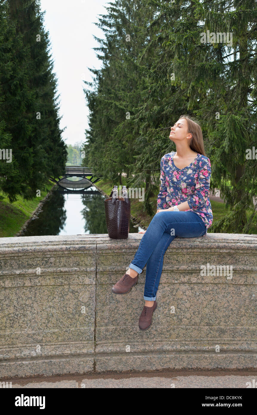 eautiful girl sits on an old stone bridge in the coniferous forest Stock Photo