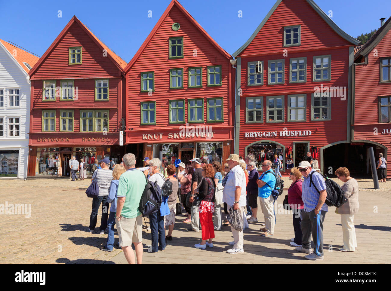 Tourists group by 14th century medieval wooden Hanseatic buildings on waterfront in old harbour district of Bryggen, Bergen, Hordaland, Norway Stock Photo