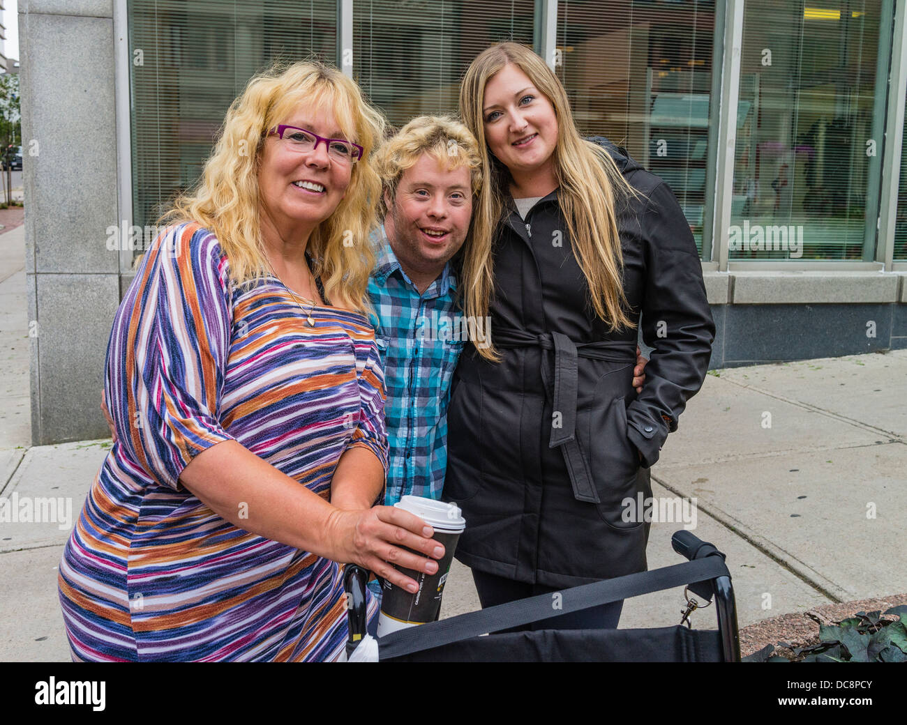 A Downs Syndrome boy smiles and stands between his mother and sister on a street in St. John, Nova Scotia, Canada. Stock Photo