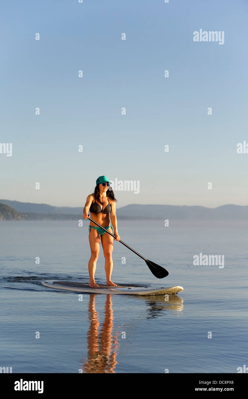 A woman, Stand Up Paddleboarding (SUP) on Lake Tahoe in the early morning on calm glassy waters, CA. Stock Photo