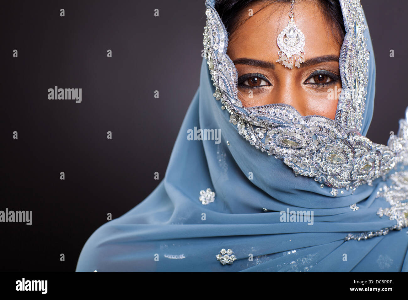 young Indian woman in sari with her face covered on black background Stock Photo
