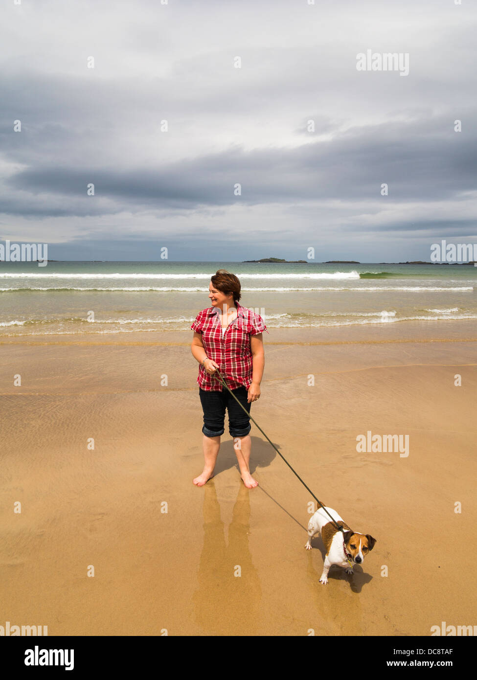 woman walking dog along beach of portrush east strand she has a jack russell terrier Stock Photo