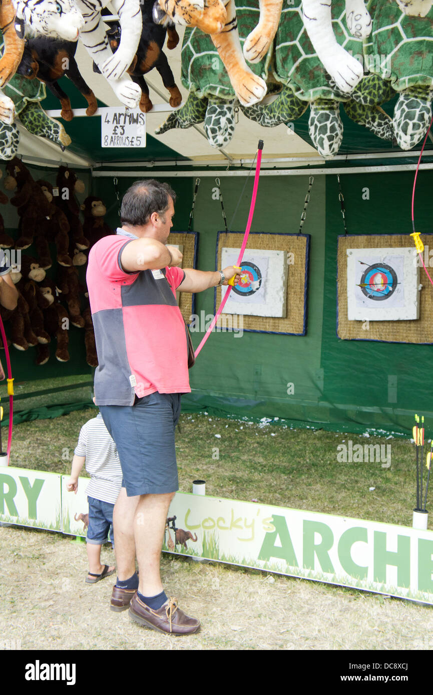 Man shooting a bow and arrow at an archery fairground stall in Swansea, Summer 2013 Stock Photo