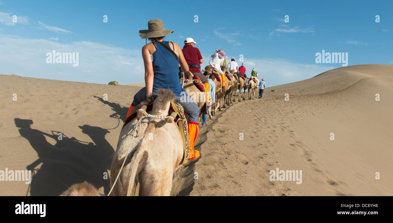 Tourists ride in a row on camels; Jiuquan, Gansu, China Stock Photo