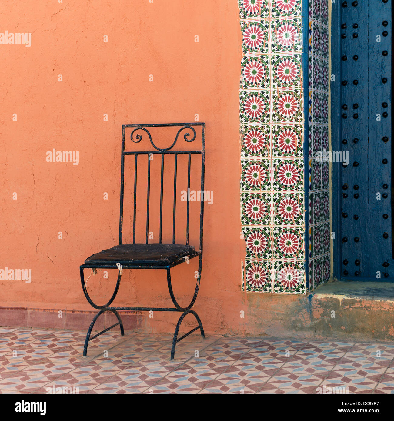 A black metal chair sits against a colourful wall; Talouste, Souss-Massa-Drass, Morocco Stock Photo