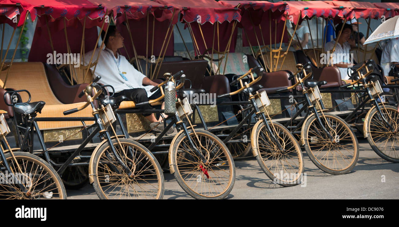 Rickshaws and a driver parked in a row in Hutong District; Beijing, China Stock Photo