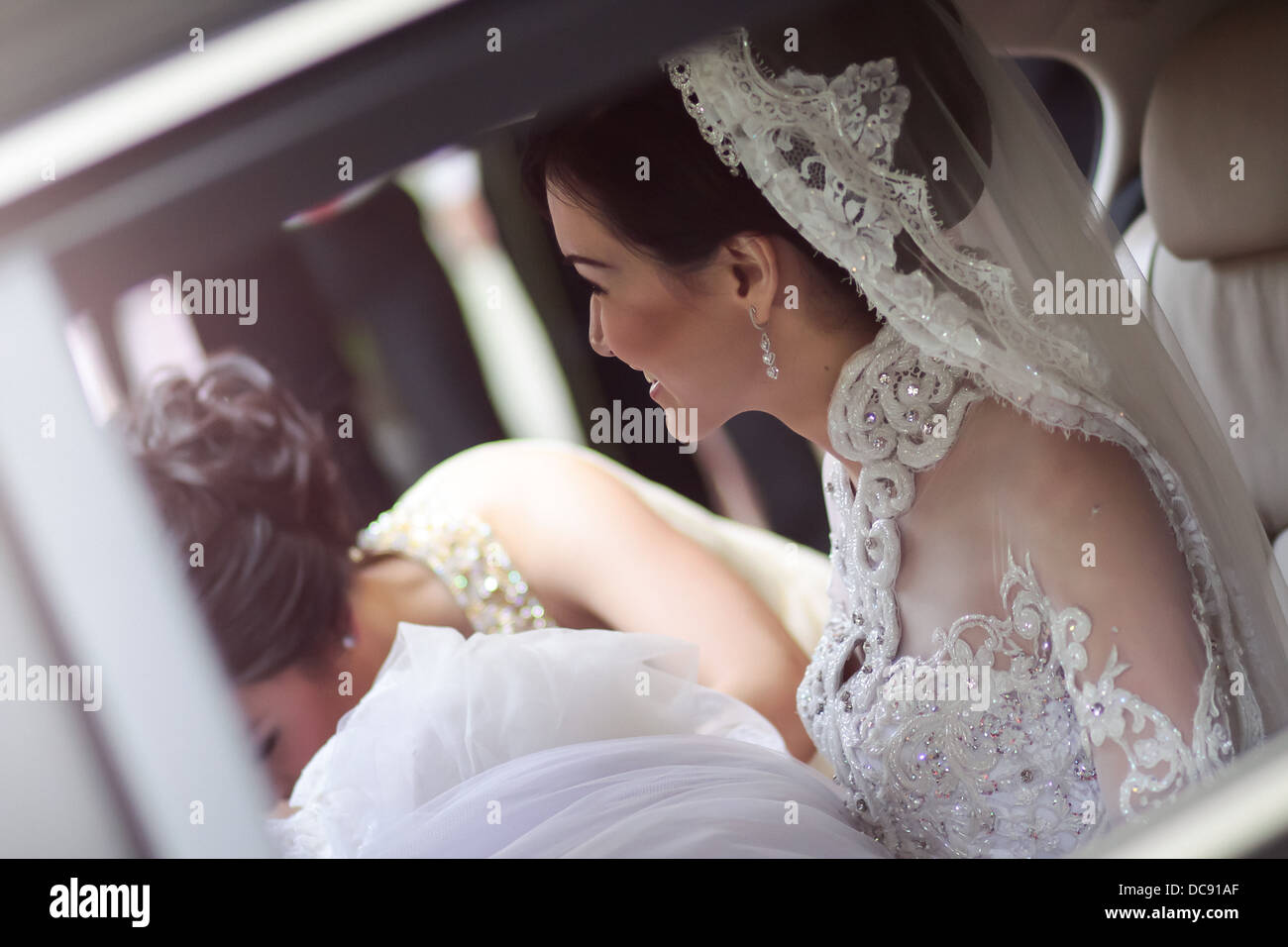 Bride sitting inside the passenger side of her wedding car while the bride's maid helping with her dress. Stock Photo