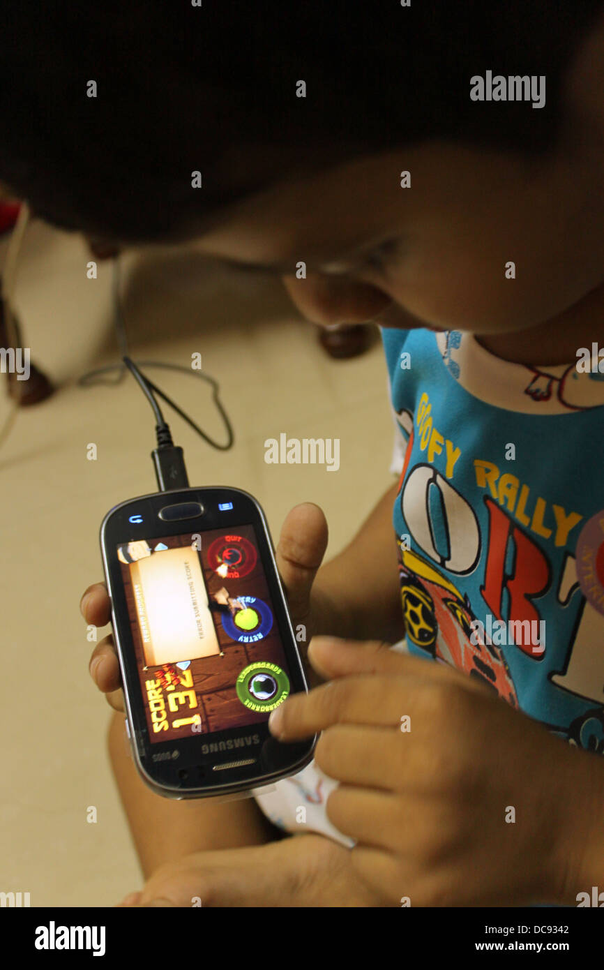Indian 4 year old toddler playing fruit ninja on a smart phone Stock Photo