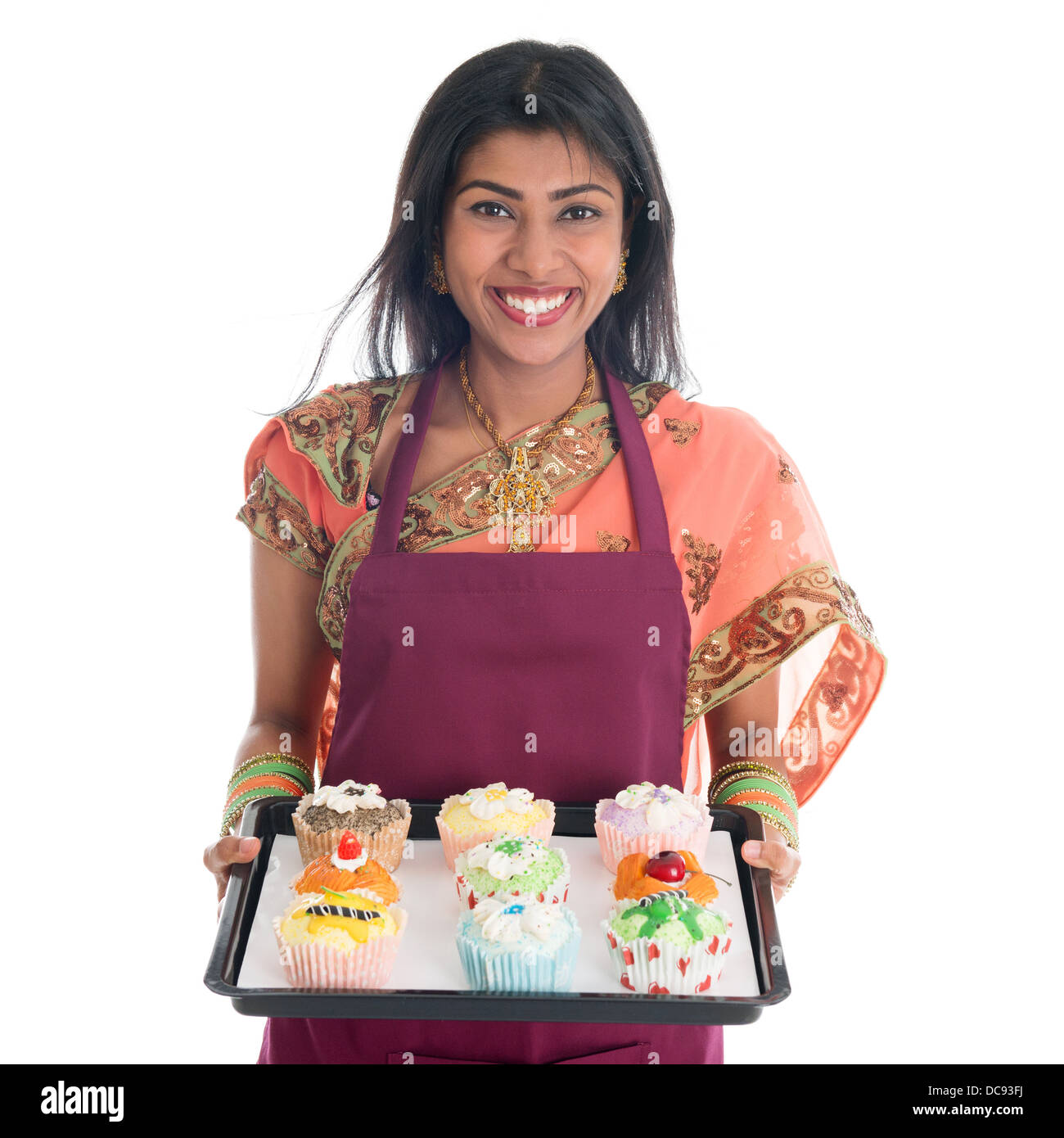 Traditional Indian woman in sari baking bread and cupcakes, wearing apron holding tray isolated on white. Stock Photo