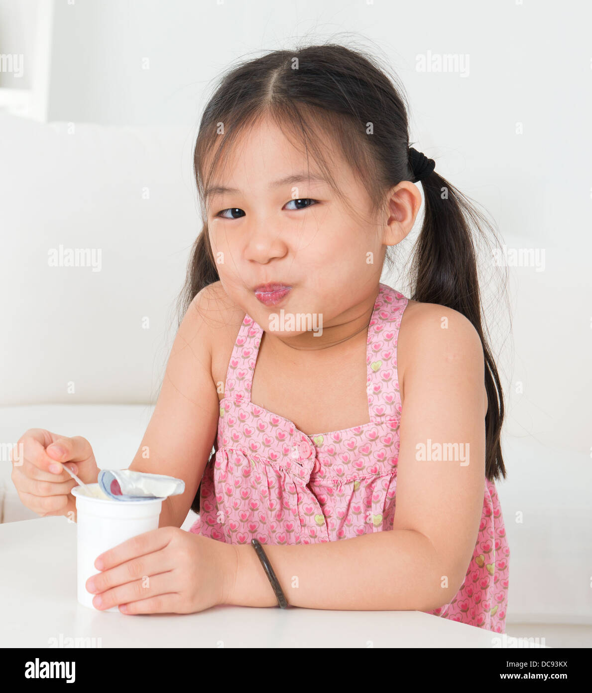 Eating yogurt. Happy Asian kid eating yoghurt at home. Beautiful child