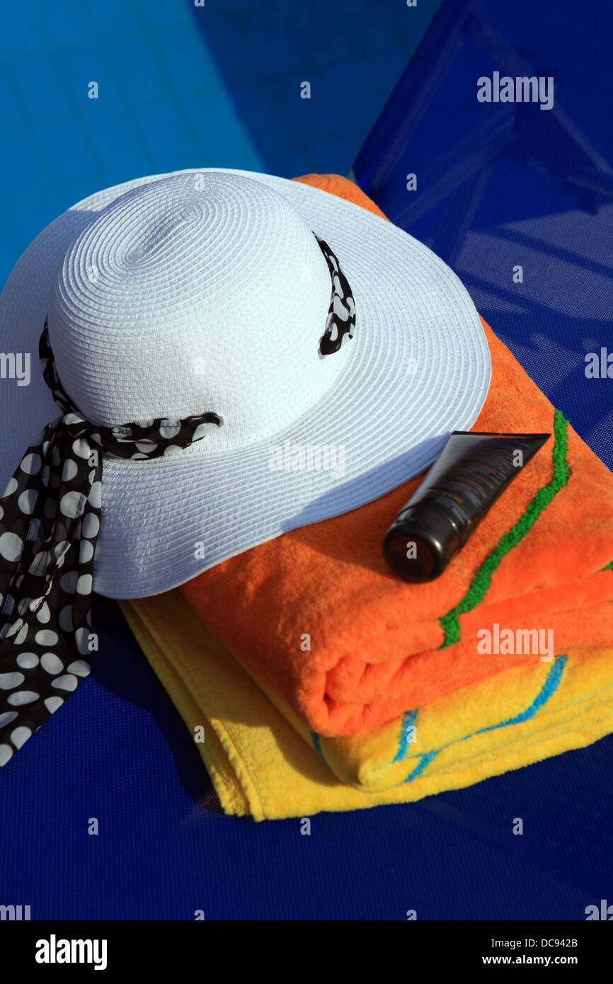 Beach towels, sun hat and sunscreen on a sun lounger by the pool Stock Photo