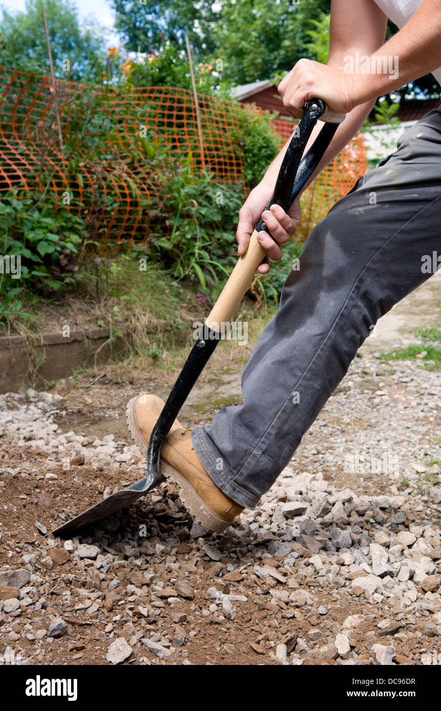 Caucasian man spreading and digging hardcore gravel in garden at home Stock Photo