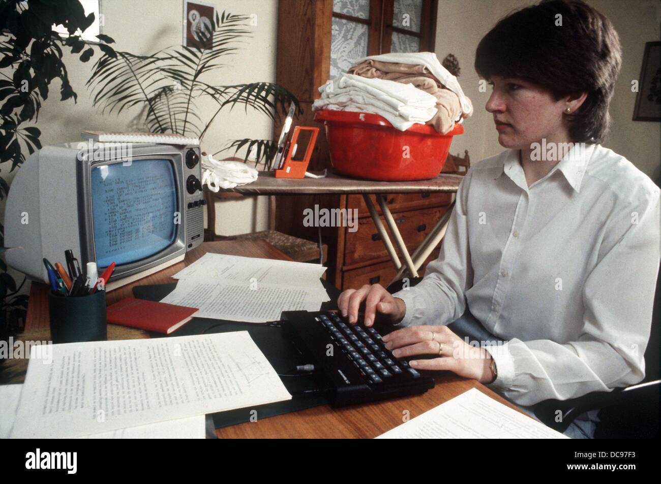 A housewife works at her computer while the ironing waits to be done in the background. Picture from 1985. Stock Photo