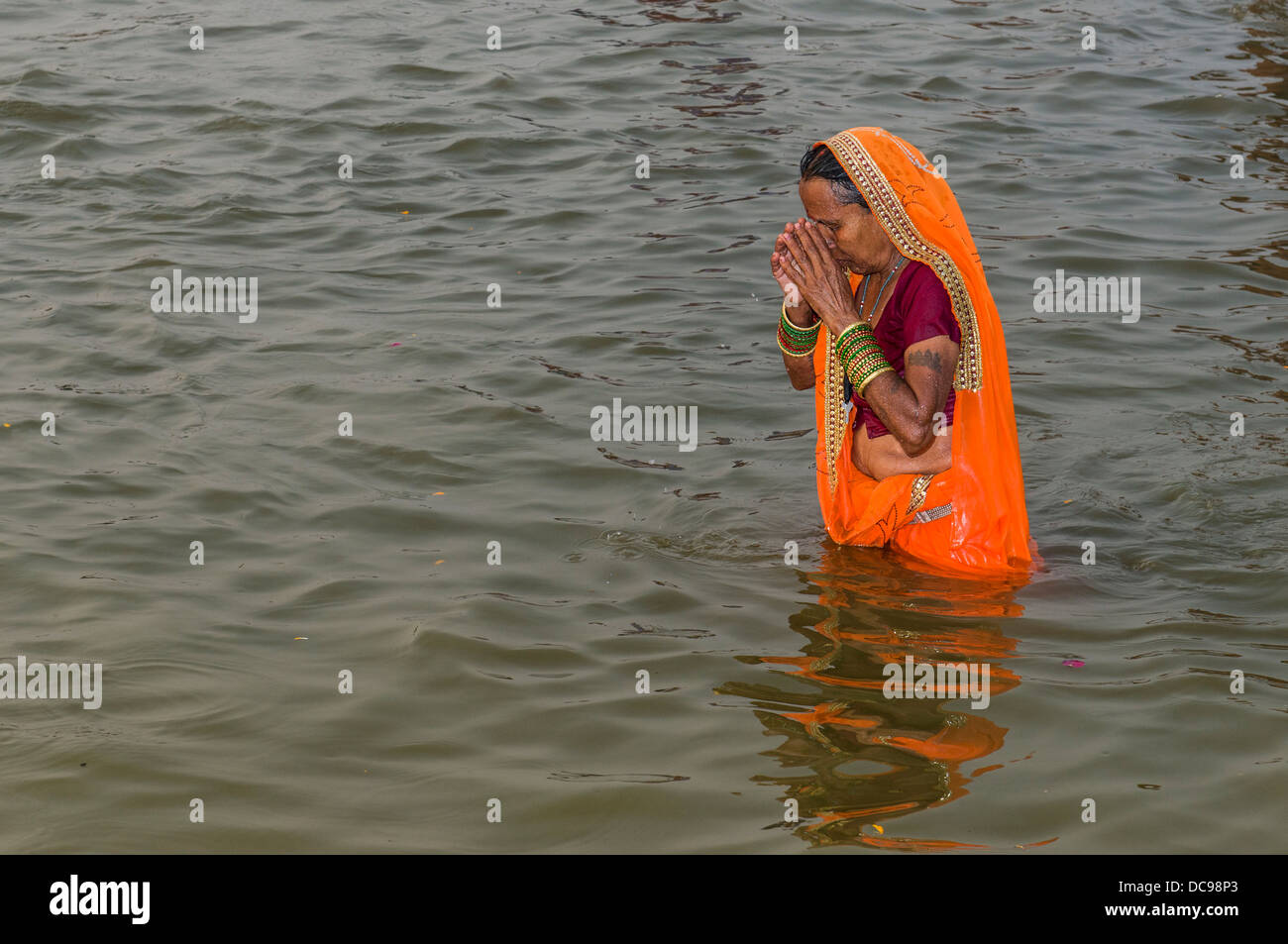 Woman wearing an orange sari taking a bath in the Sangam, the confluence of the rivers Ganges, Yamuna and Saraswati, in the Stock Photo