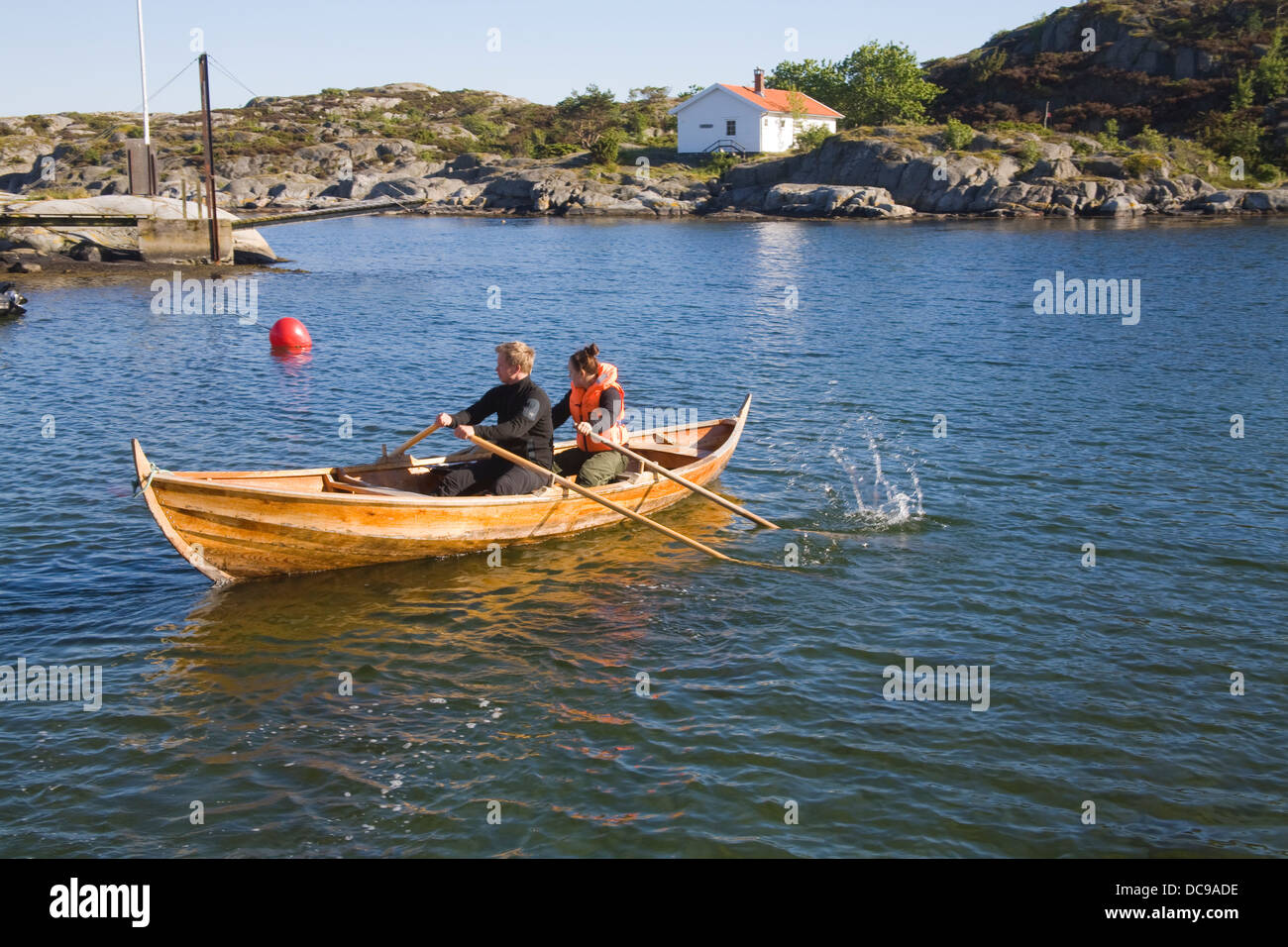 Høvåg Norway Europe Young man and girl rowing boat across calm water of sheltered harbour Stock Photo