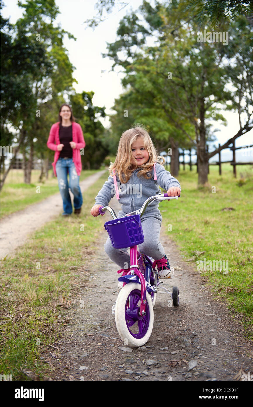 Cute toddler girl on her 1st bicycle with her mom running behind her. Also available in a black & white photo. Stock Photo