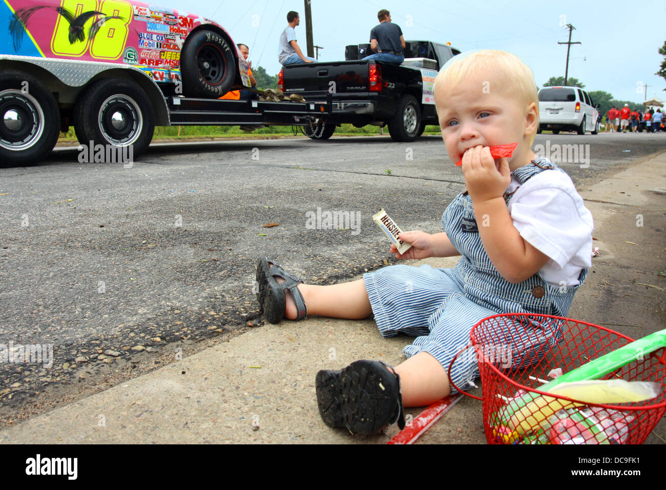 a cute baby boy is sitting on the side of the street eating candy at a parade in Bangor, Wisconsin. Stock Photo