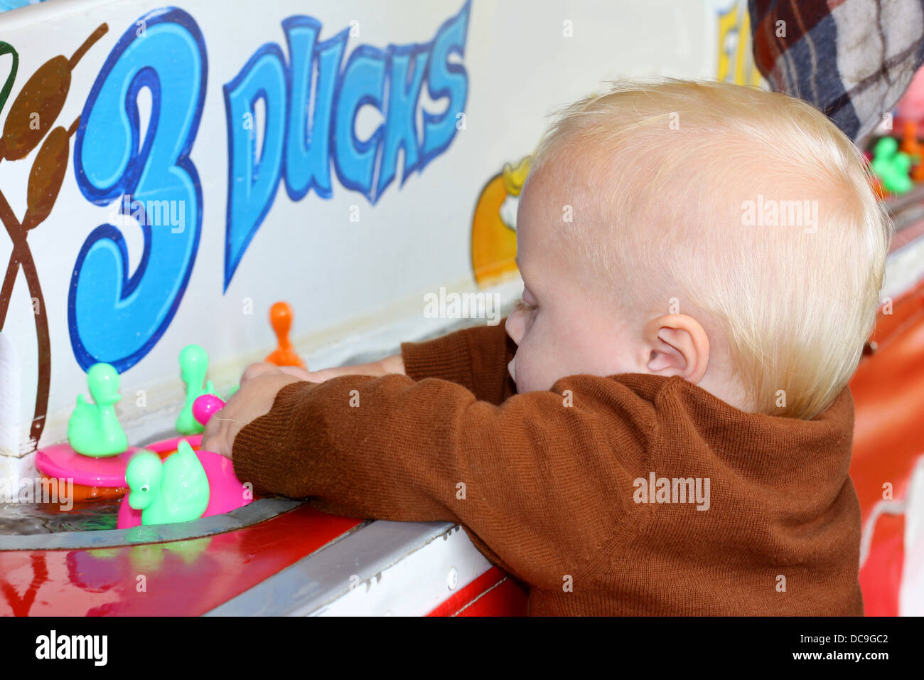 a cute baby boy is grabbing a handful of ducks as they float by during a summer carnival duck game Stock Photo