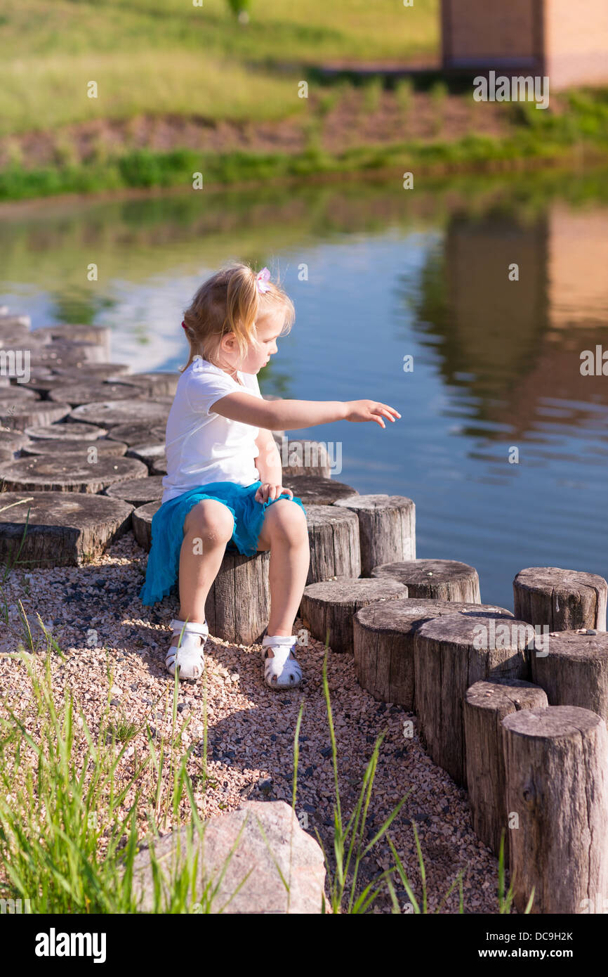 Cute little girl sitting near the lake in summertime in nature Stock ...