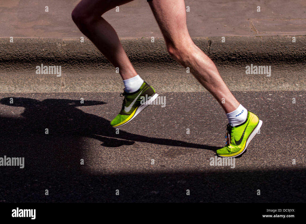 Athlete taking part in a race running by with shadow falling on to the road Stock Photo