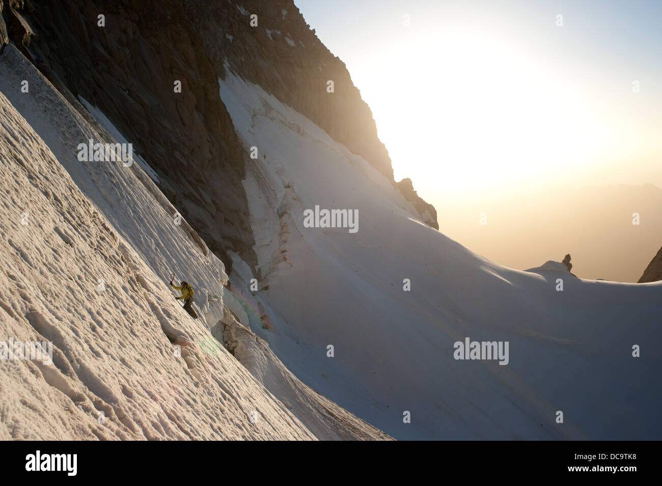 Alpinist climbing snow slope. Sunshine and snow crest is visible in background. Stock Photo
