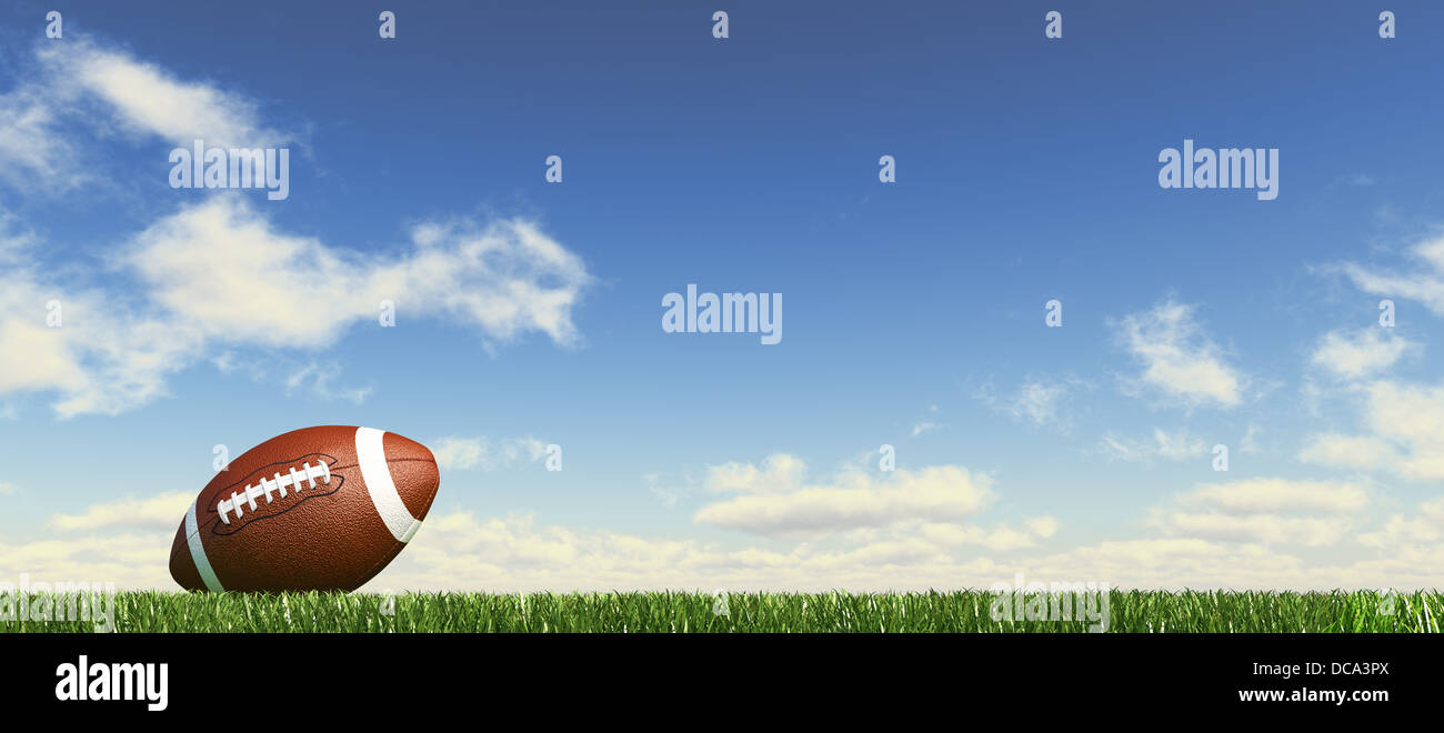 American football ball, on the grass, with fluffy clouds sky in the background. Side view, from ground level, panoramic format. Stock Photo