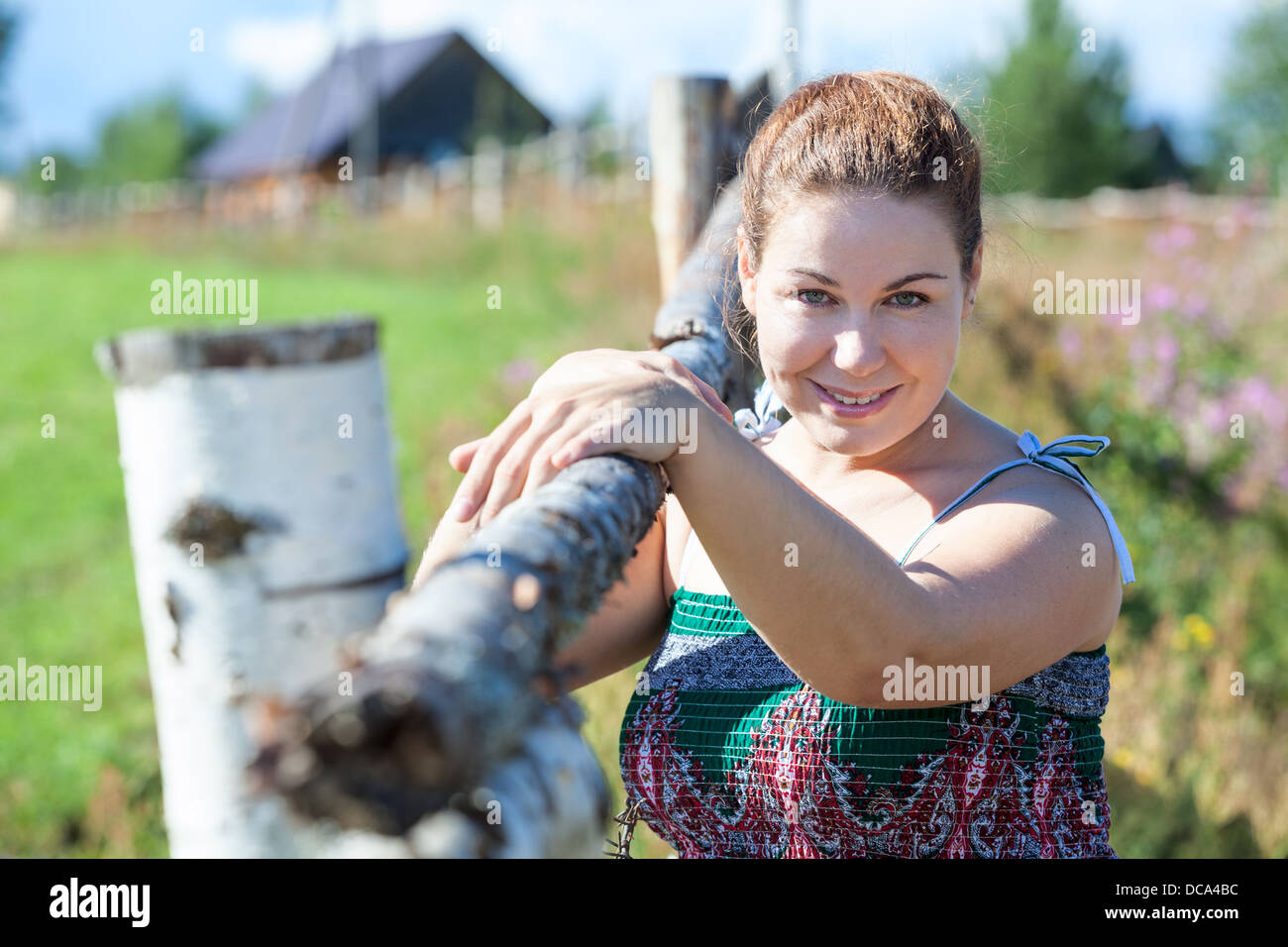 Attractive village woman in sundress posing near fence. Russian people