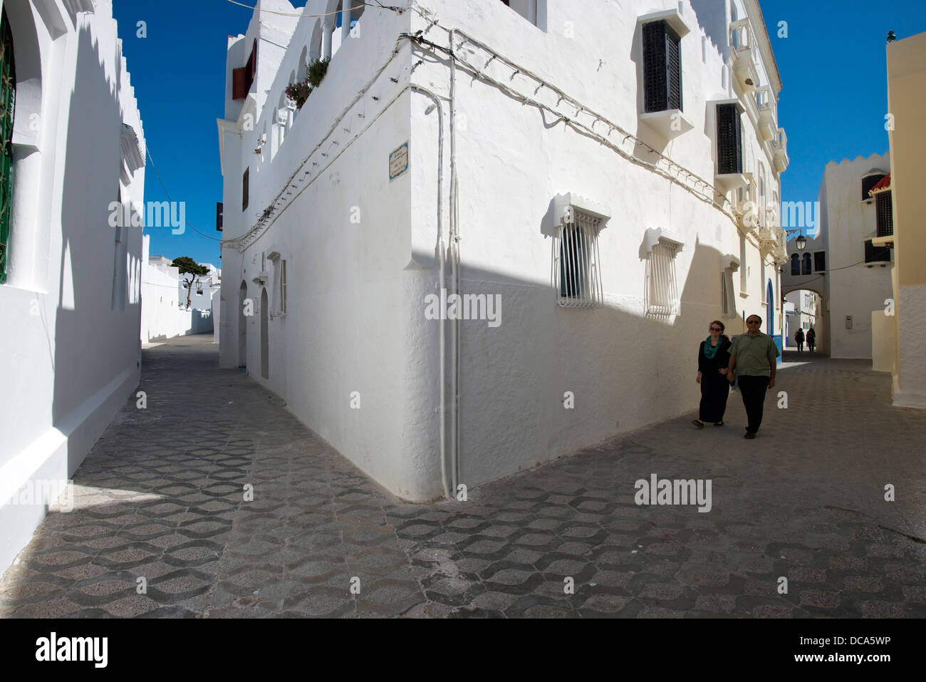 A man and woman walk down a street in the coastal town of Asilah, Morocco. Stock Photo