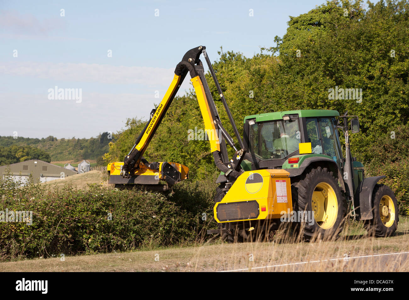 Green and Yellow John Deer tractor with hedge cutting arm in action trimming a hedge at the edge of a field in Oxfordshire, UK. Stock Photo