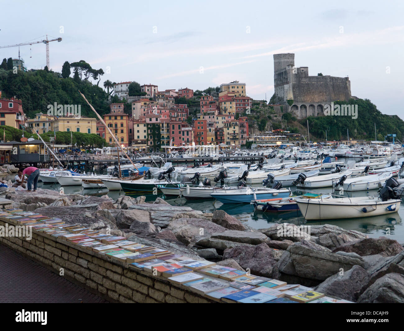 Boats in the harbour, with books and rocks in the foreground and a castle in the background, Lerici, La Spezia, Italy Stock Photo