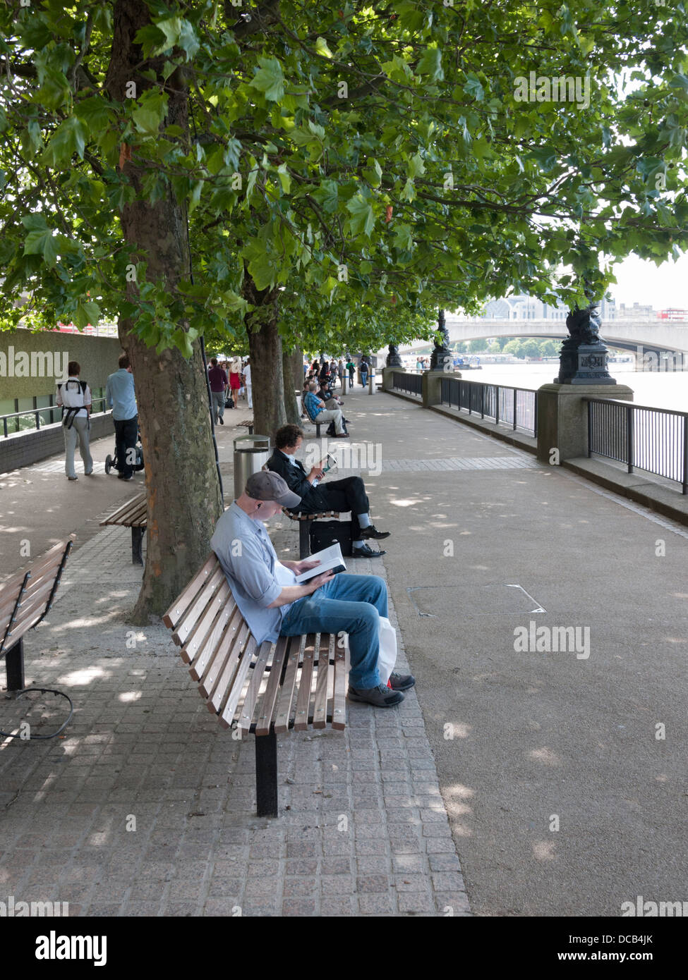 People sitting on benches reading on the Southbank London UK on a summer day Stock Photo
