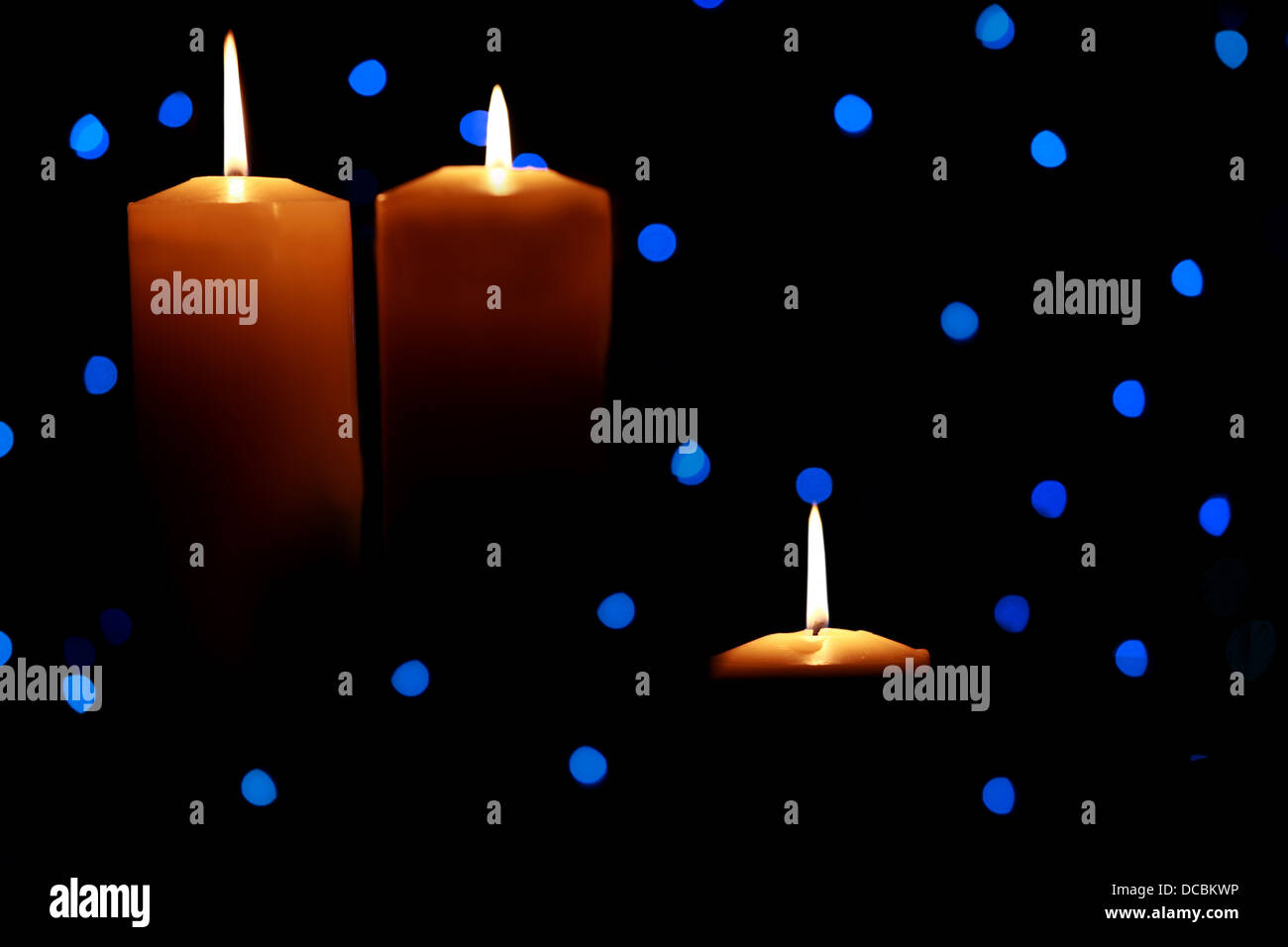Three large candles lit amongst blue lights Stock Photo Alamy