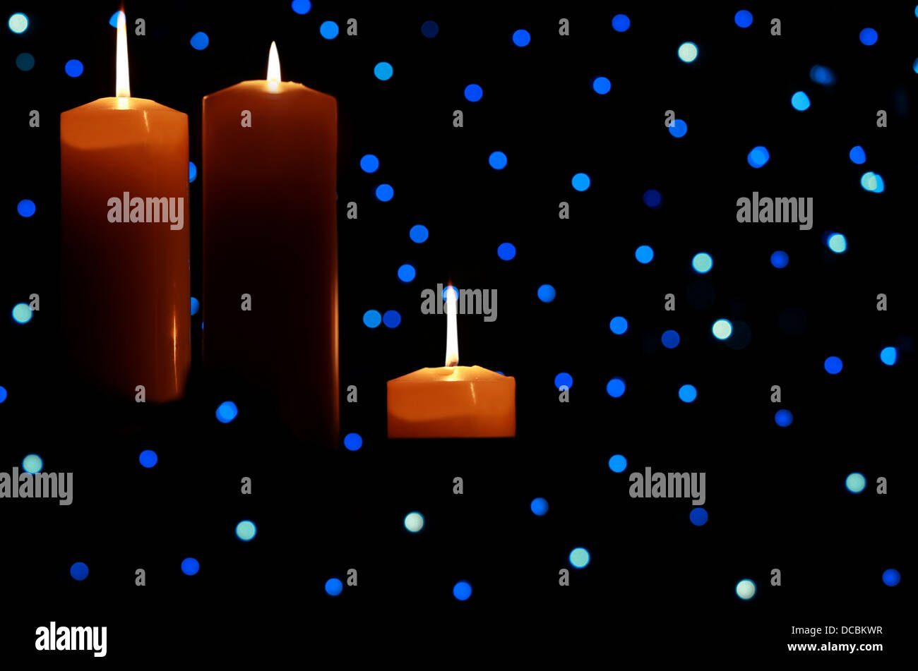 Three large candles lit amongst blue lights Stock Photo Alamy