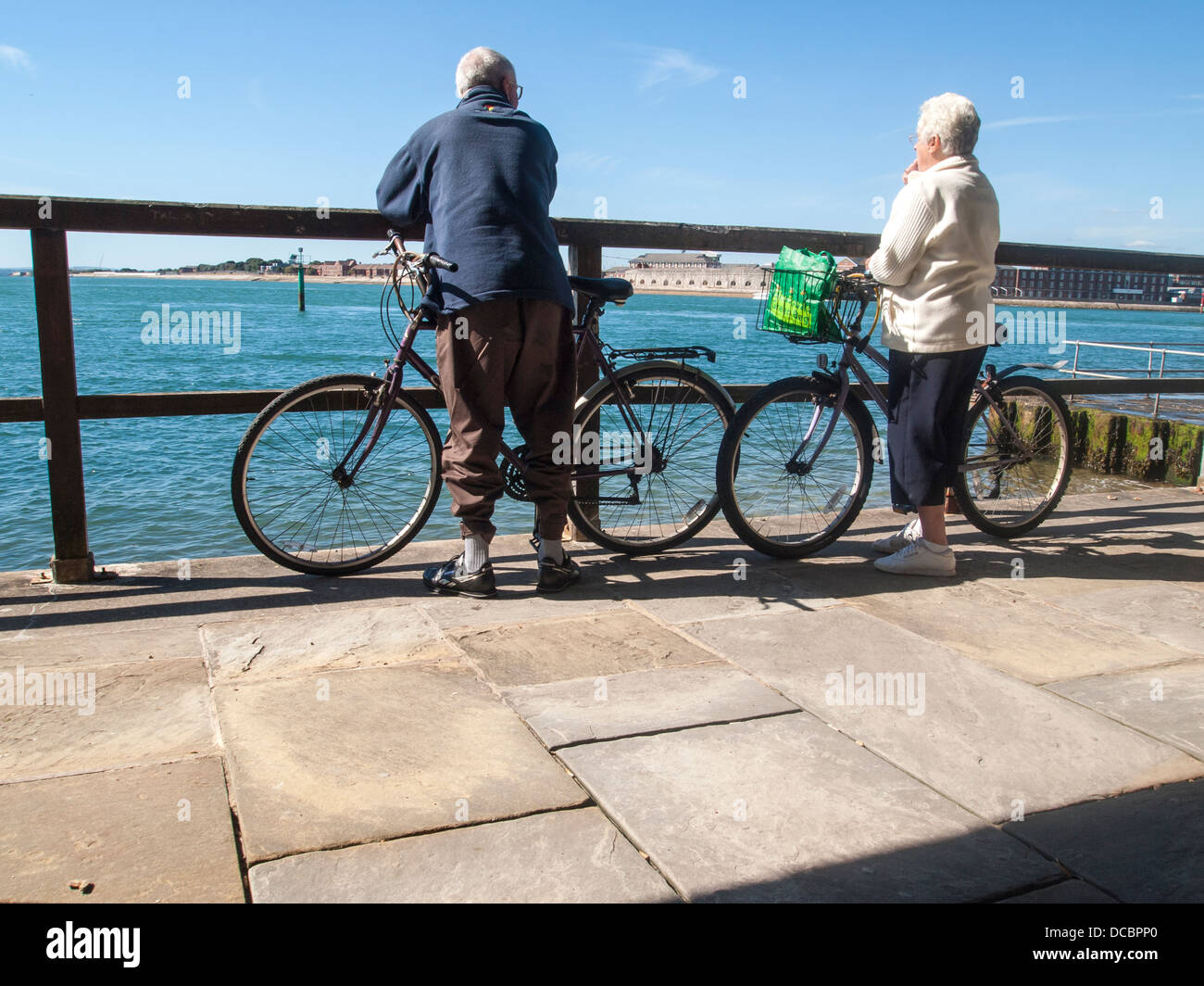 a male and female senior couple with bicycles stand looking out to sea in Portsmouth, Hampshire Stock Photo