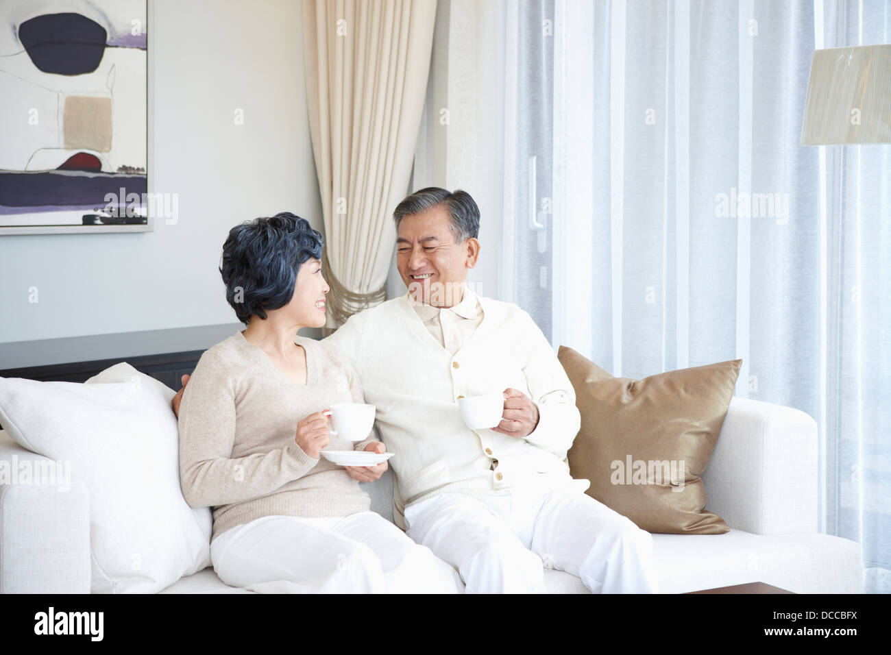 middle aged couple sitting on a couch drinking coffee Stock Photo - Alamy