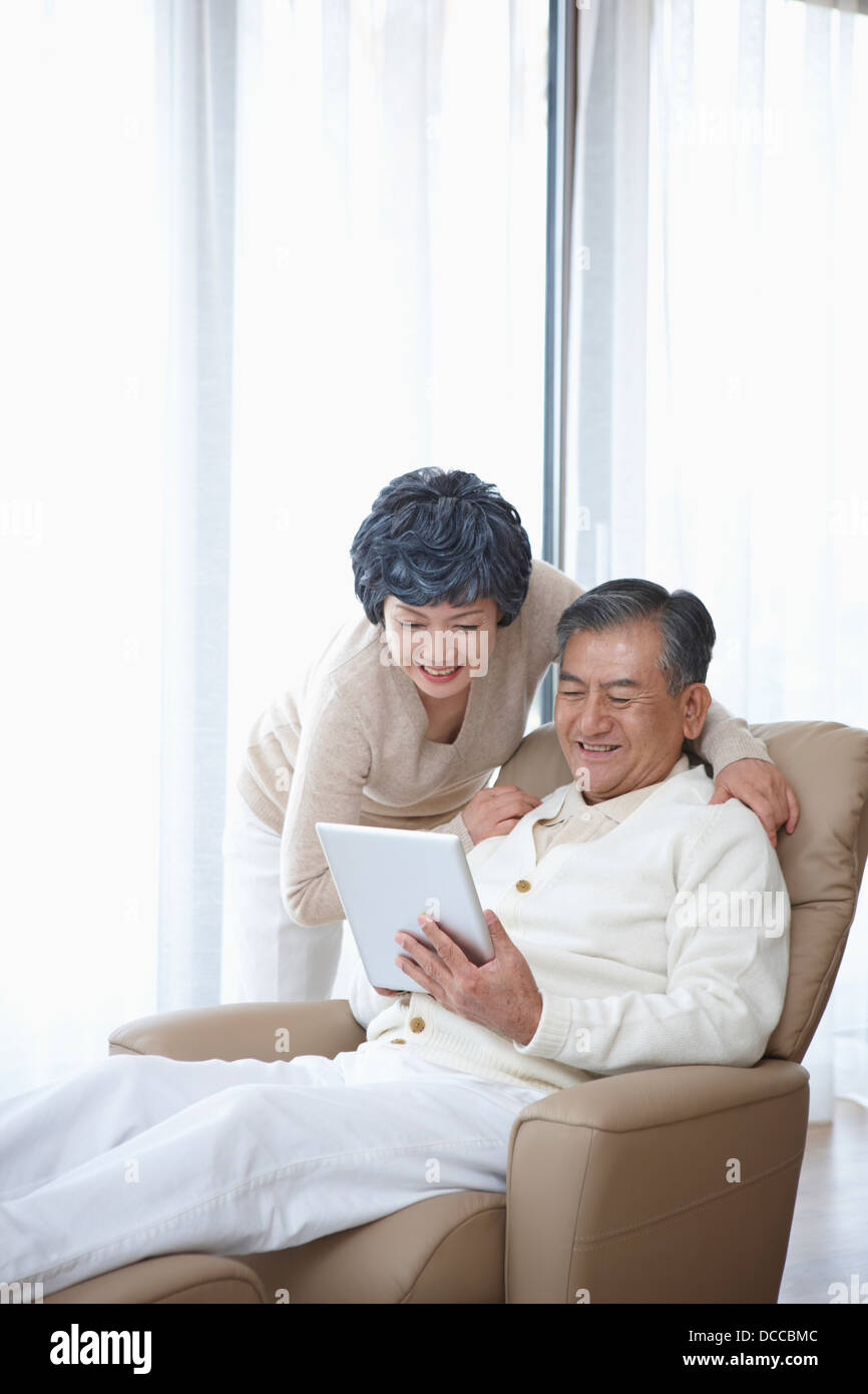 wife standing next to a middle aged man sitting on a lazy boy chair Stock Photo
