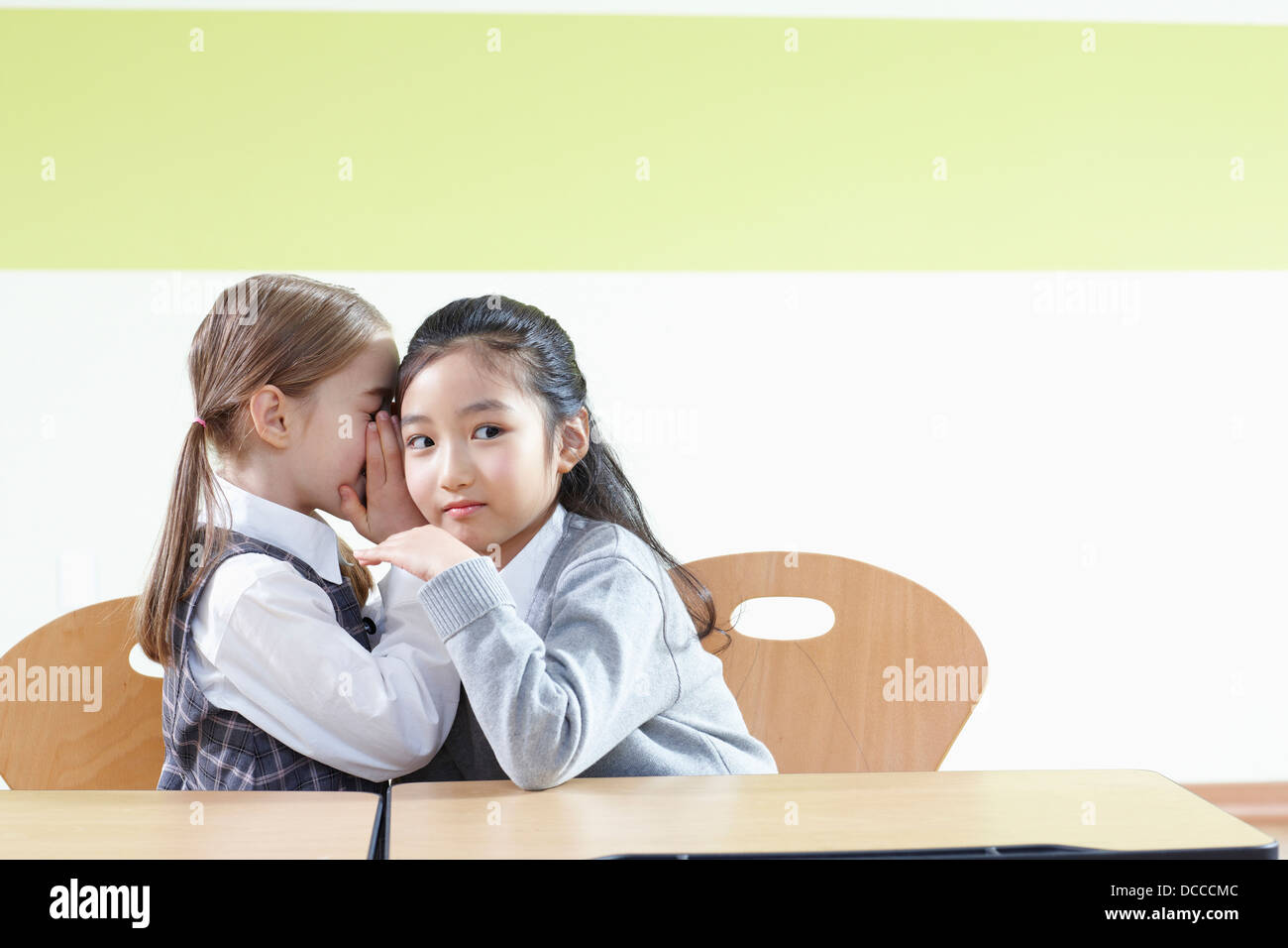 a girl whispering to her friend in a classroom Stock Photo - Alamy