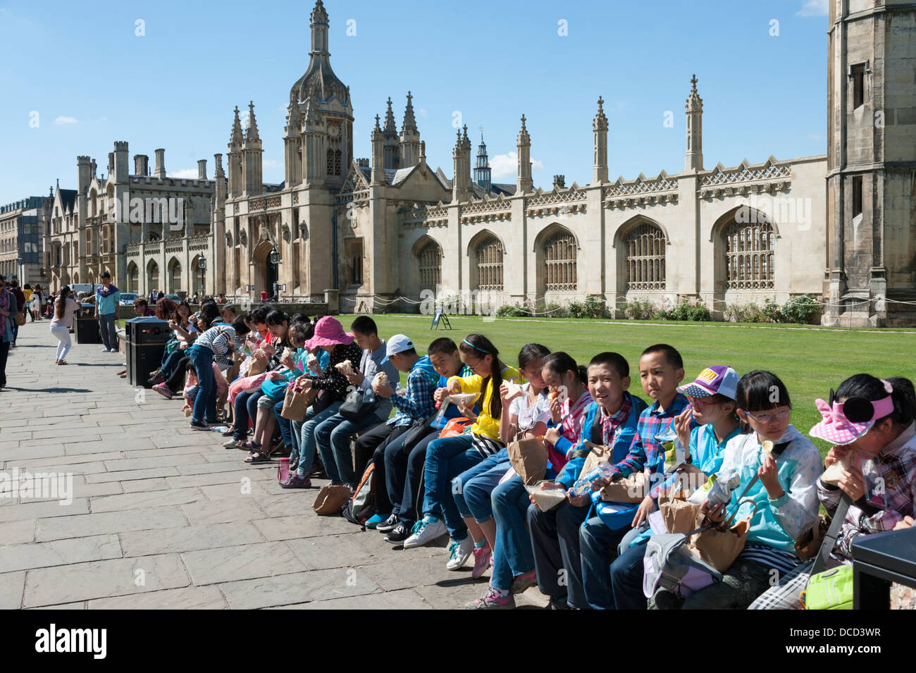 Young chinese children tourists lined up on a wall outside King's College Cambridge UK having lunch or picnic Stock Photo