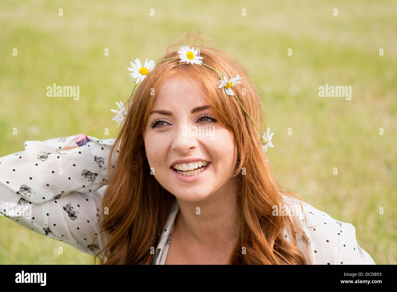 A horizontal, colour image of a happy, young, smiling woman with long red hair, with a daisy chain in her hair Stock Photo
