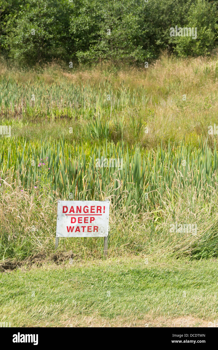 Danger Deep Water sign sited near what appears to be an innocuous relatively shallow pond. Deceptively so? Stock Photo