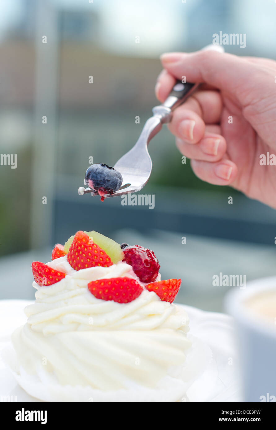 White creamy cake with strawberries and female hand holding fork Stock Photo