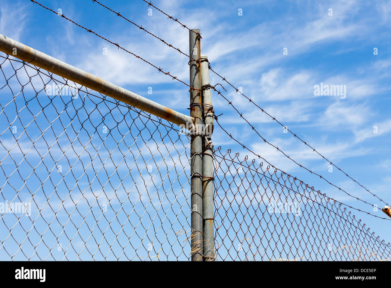 Mesh fence with barbed wire on a background of blue sky Stock Photo