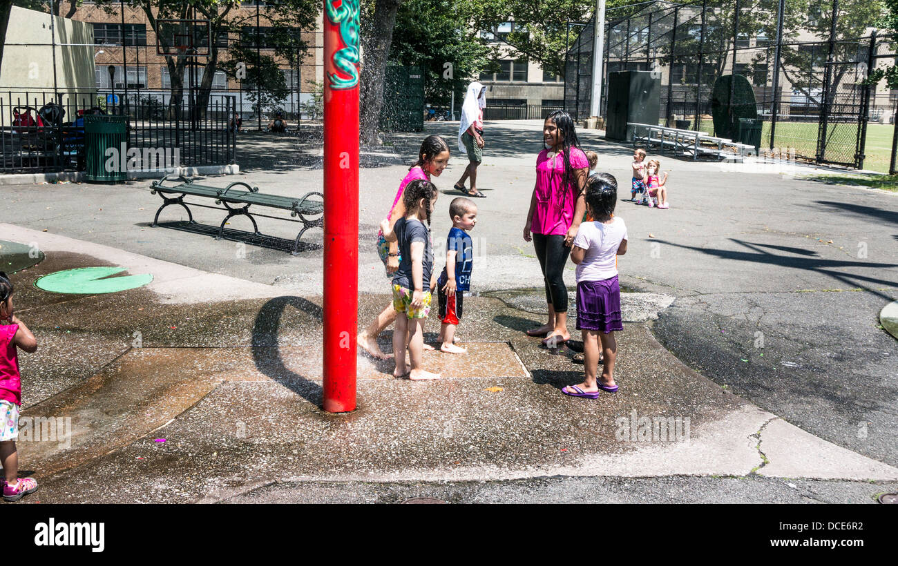 multiethnic group of children in soaking wet street clothing enjoy water feature of DeWitt Clinton park on hot summer day NYC Stock Photo