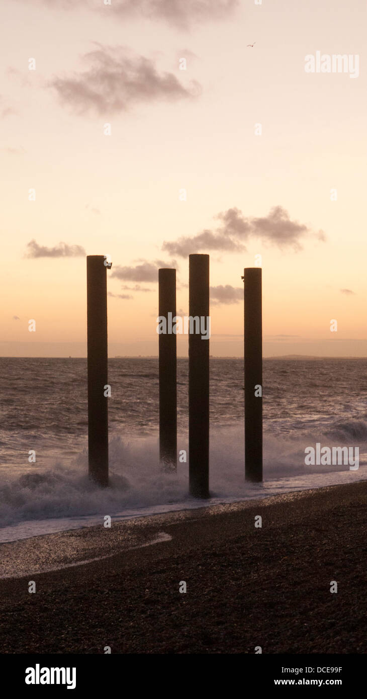 Four poles emerging from the waves on a beach, at dusk. Stock Photo