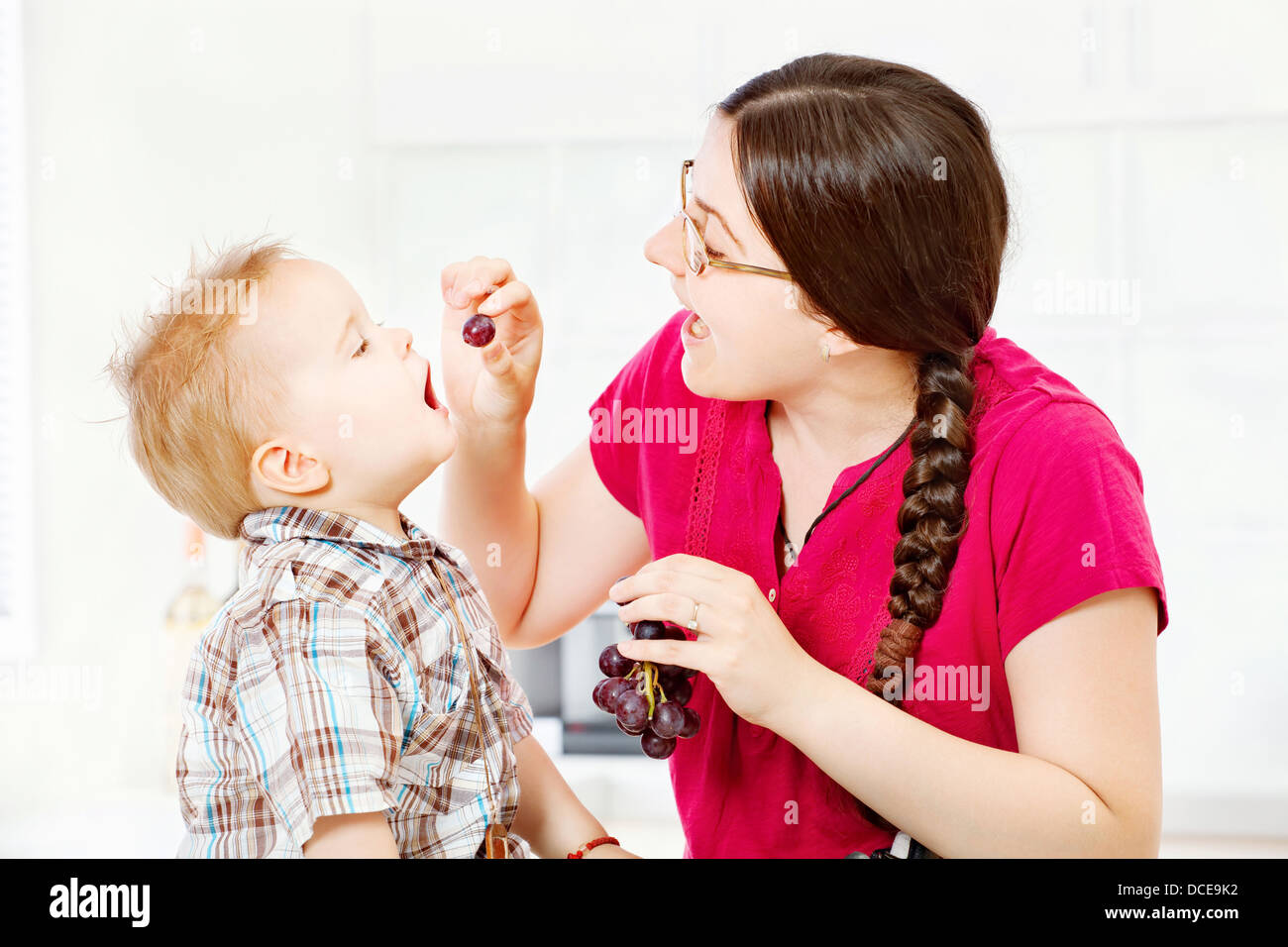 Mother feeding child with grapes in kitchen Stock Photo Alamy