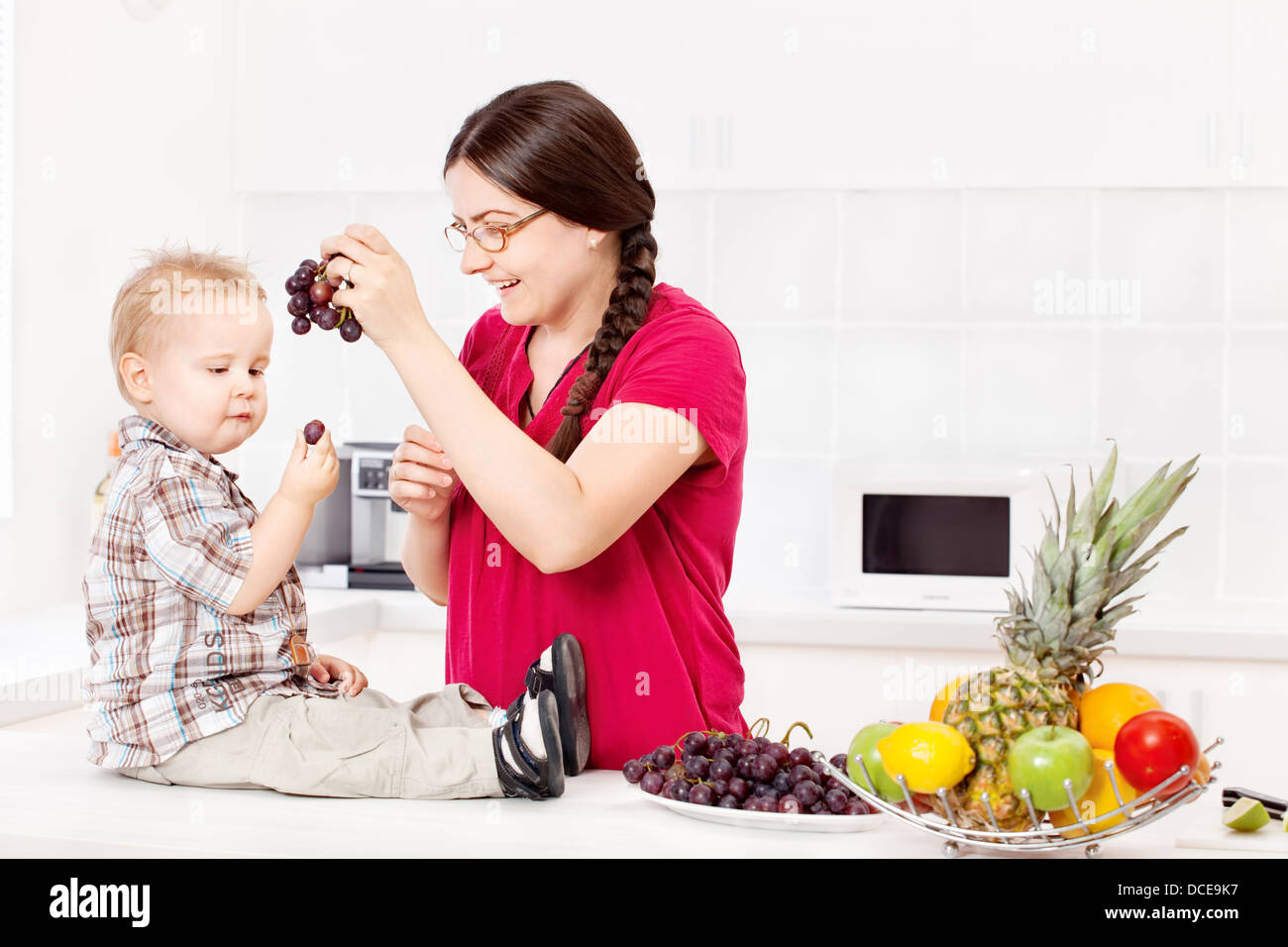 Mother feeding child with grapes in kitchen Stock Photo Alamy