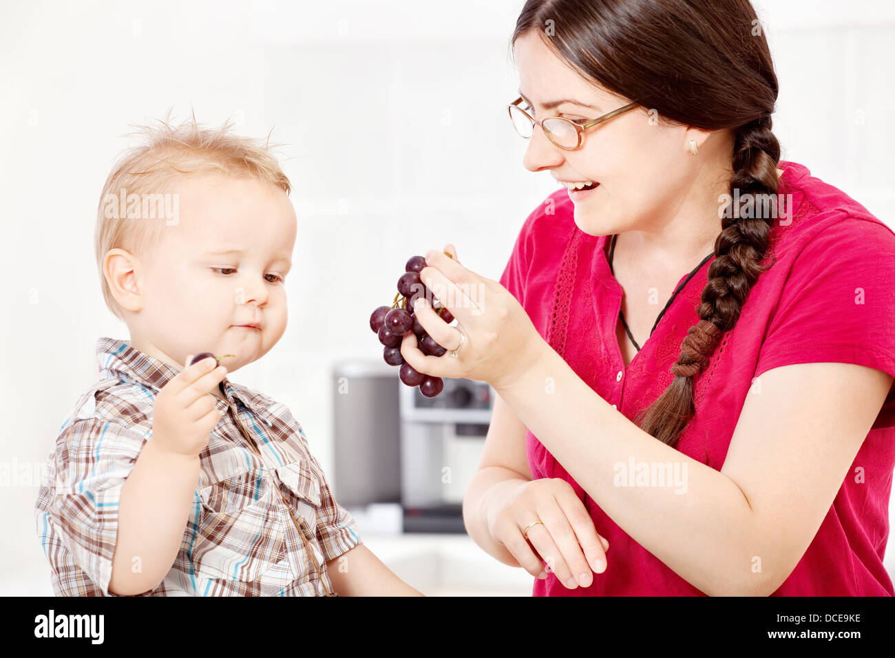 Mother feeding son with grapes in kitchen Stock Photo Alamy
