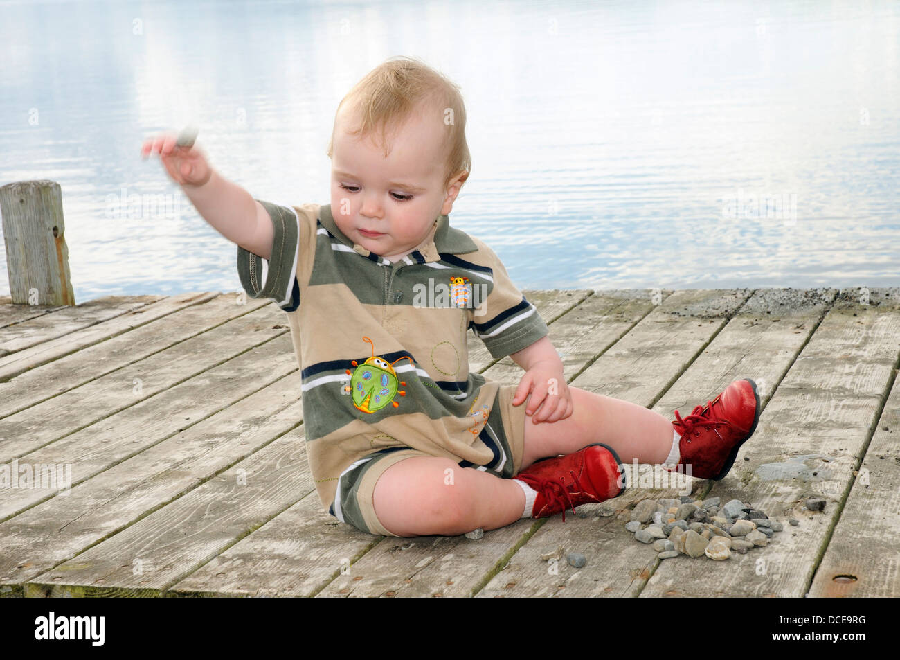 A small boy (aged 15 months) playing with a pile of stones Stock Photo