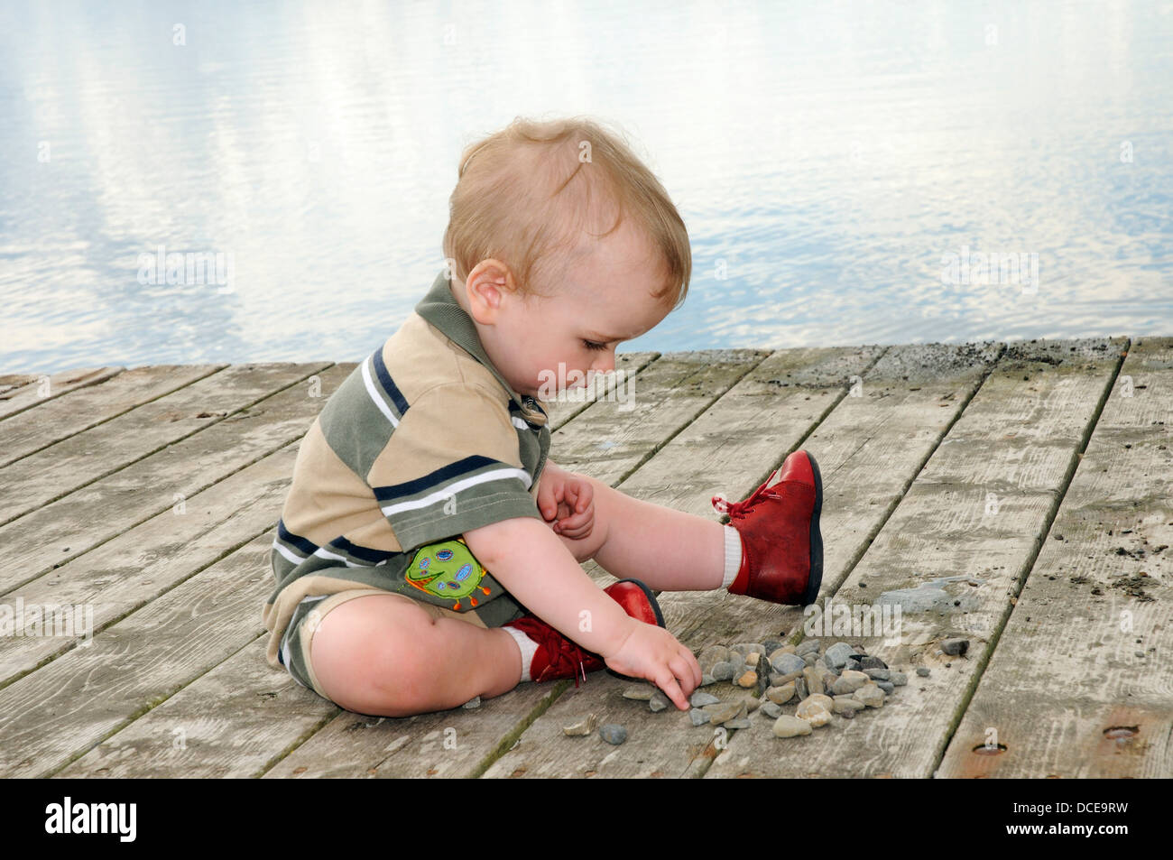 A small boy (aged 15 months) playing with a pile of stones Stock Photo