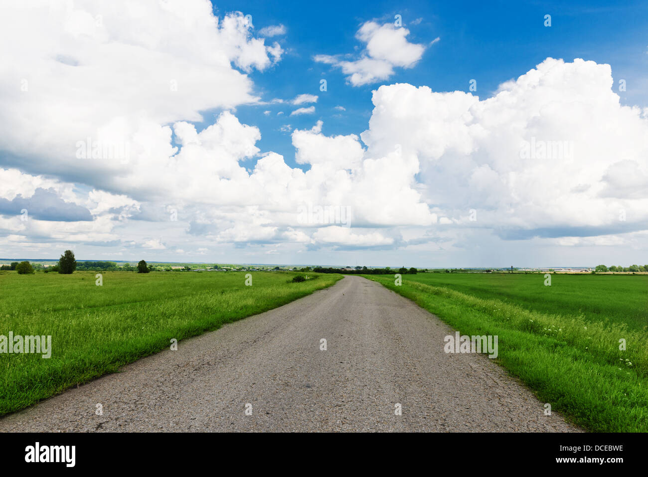 asphalt road through the green field and clouds on blue sky in summer ...